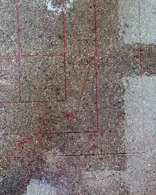Top-down view of speckled concrete with thin red lines in a rectangular pattern, some areas darker and glossier than others.