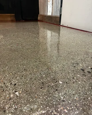 Low-angle view of a glossy speckled concrete floor with visible stone chips, running to a white door and corrugated metal wall panels.