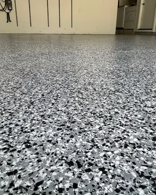Low-angle view across a black, white and gray flake garage floor toward cream walls, a hanging hose and an open doorway.