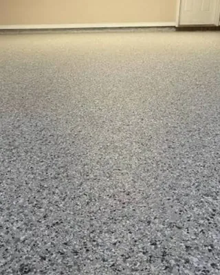 Low-angle view of a gray, black and white flake floor running to a beige wall and a white door.