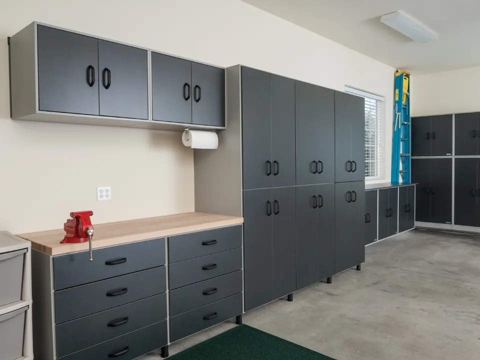 Garage wall lined with dark gray cabinets and a workbench with drawers, a wooden top and a red vise
