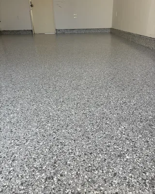 Gray, black and white flake garage floor with matching coated stem walls along beige walls, and a door at the back left.