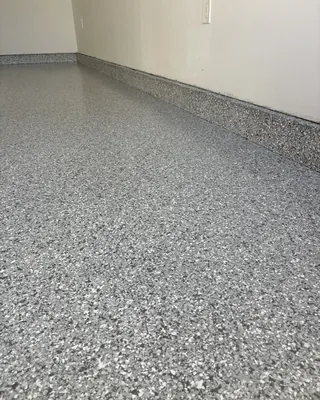 Gray flake garage floor meeting a flake-coated stem wall along a beige wall with a light switch.