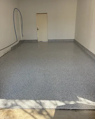 Single-bay garage with a gray flake floor and coated stem walls, a door at the back and a blue hose on the left wall.
