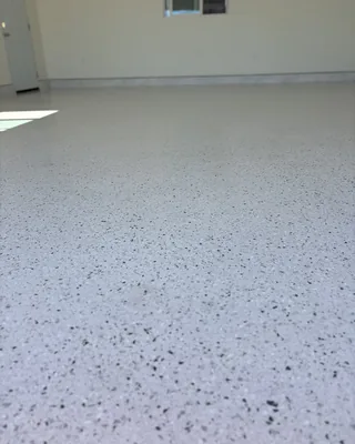 Light gray garage floor with fine black and gray flecks, a white door on the left and a window in the back wall.