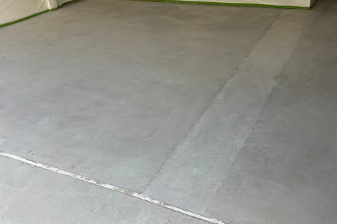 Bare, ground concrete garage floor with joint lines, the walls masked with plastic sheeting and green tape.
