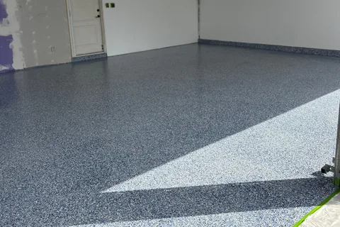 Blue, gray and white flake garage floor with sunlight across it, white walls and a door at the back left.
