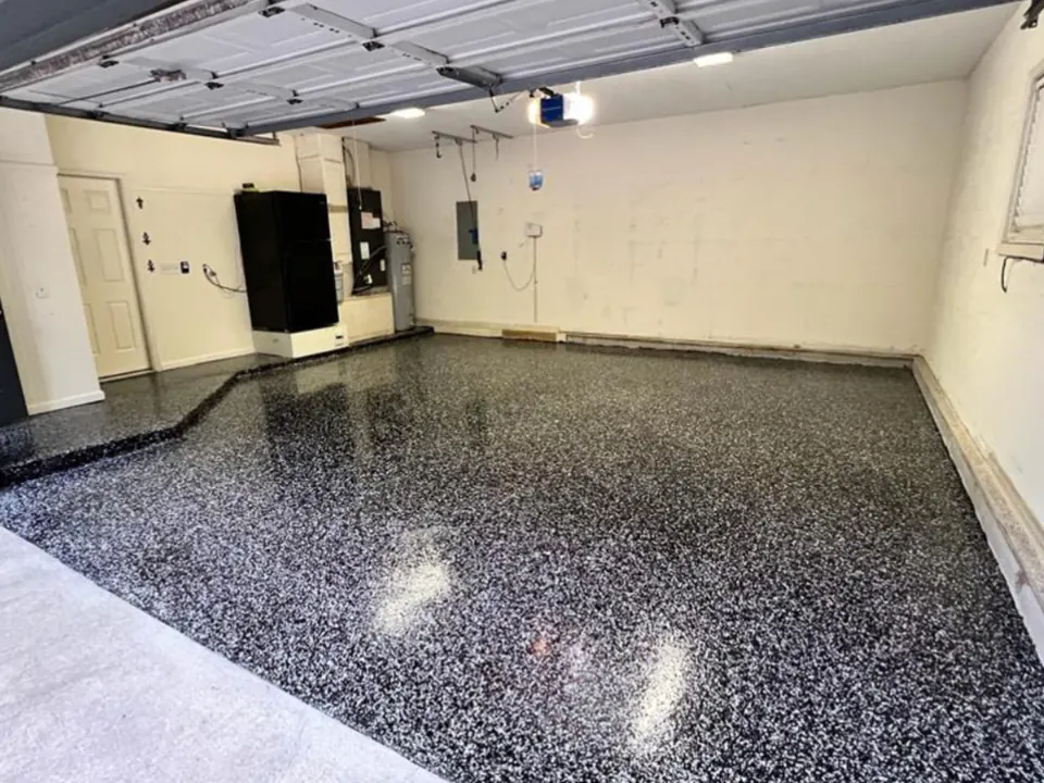 Two-car garage with a glossy black and white flake floor, and a black refrigerator and water heater along the back wall.