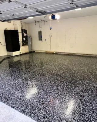 Two-car garage with a glossy black and white flake floor, and a black refrigerator and water heater along the back wall.