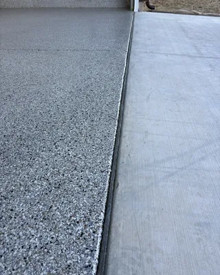 Straight edge where a gray, black and white flake garage floor meets the uncoated concrete driveway.