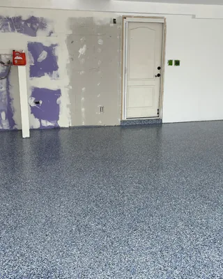 Blue, gray and white flake garage floor in front of a wall with patched drywall and a white door.