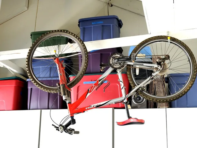 Storage rack mounted under a garage ceiling holding colored plastic bins, with a bicycle hanging below it