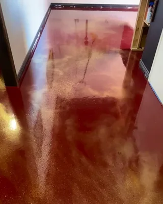 Glossy deep red floor with swirls of gold shimmer in a narrow room with white walls and a wooden shelf unit.