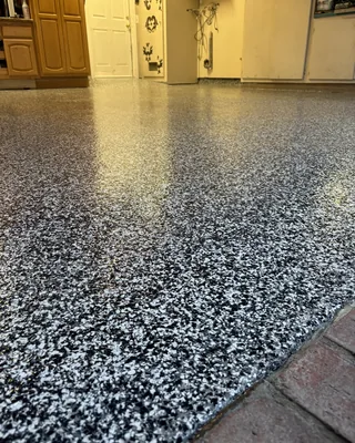 Glossy black and white flake garage floor meeting red brick pavers in front, with wooden cabinets and a white door at the back.