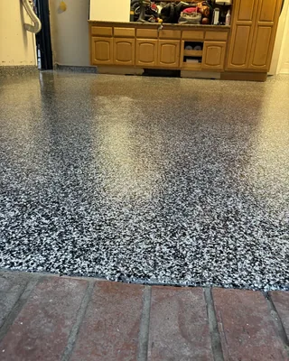 Black and white flake garage floor behind a red brick threshold, with wooden base cabinets and items on the counter at the back.