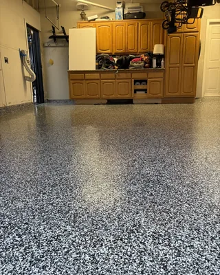 Black, white and gray flake garage floor in front of wooden cabinets, with a white door on the right.