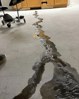 A long crack in a bare concrete garage floor filled with dark, wet-looking material, with wooden cabinets at the back.
