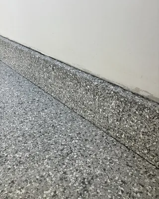 Low stem wall along the base of a white garage wall, coated in the same gray, black and white flakes as the floor.