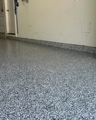 Gray, black and white flake garage floor with coated stem walls along cream walls, and a white cabinet and door at the back left.