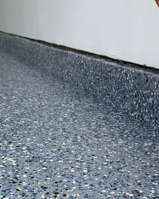 Close-up of a stem wall and floor coated with blue, gray, white and black flakes, with an orange cord running down the white wall.