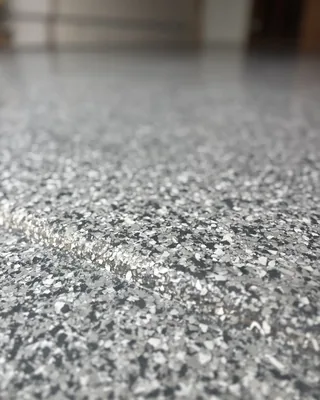 Close-up of gray, black and white flakes in a glossy floor, with the coating carried over a small step in the floor.