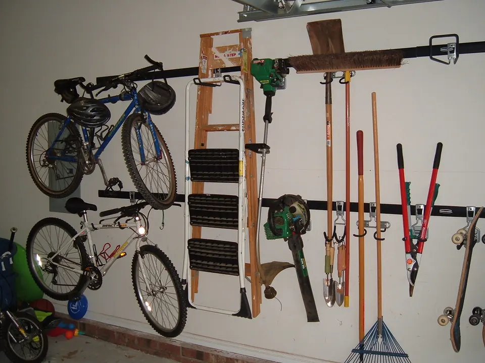 Bicycles, a stepladder and long-handled yard tools hanging from hooks on a rail along a garage wall