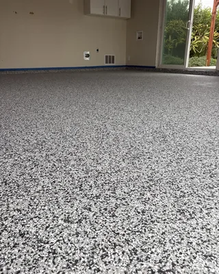 Black, gray and white flake floor in a beige-walled room with a white wall cabinet and a sliding glass door to a garden.