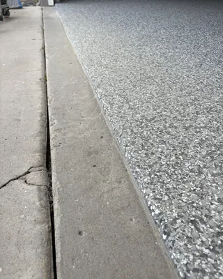 Edge of a gray flake garage floor meeting the uncoated concrete driveway, with the coating wrapped over the rounded slab edge.